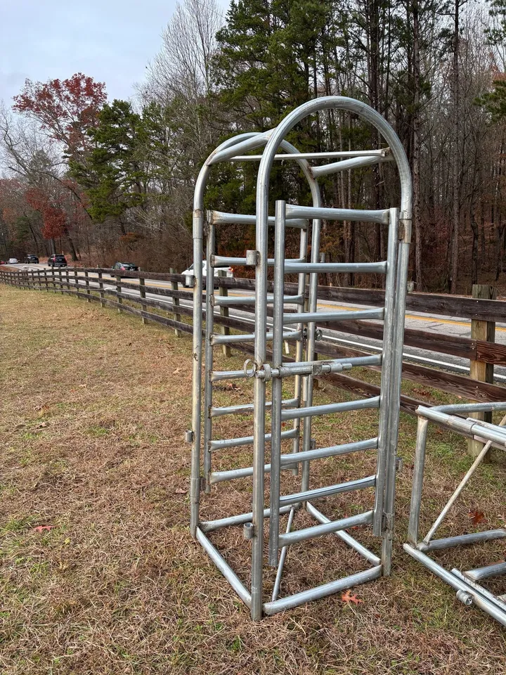 Galvanized palpation cage standing upright beside a fence