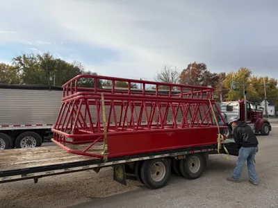 Red double bale feeder with insert loaded on a flatbed trailer