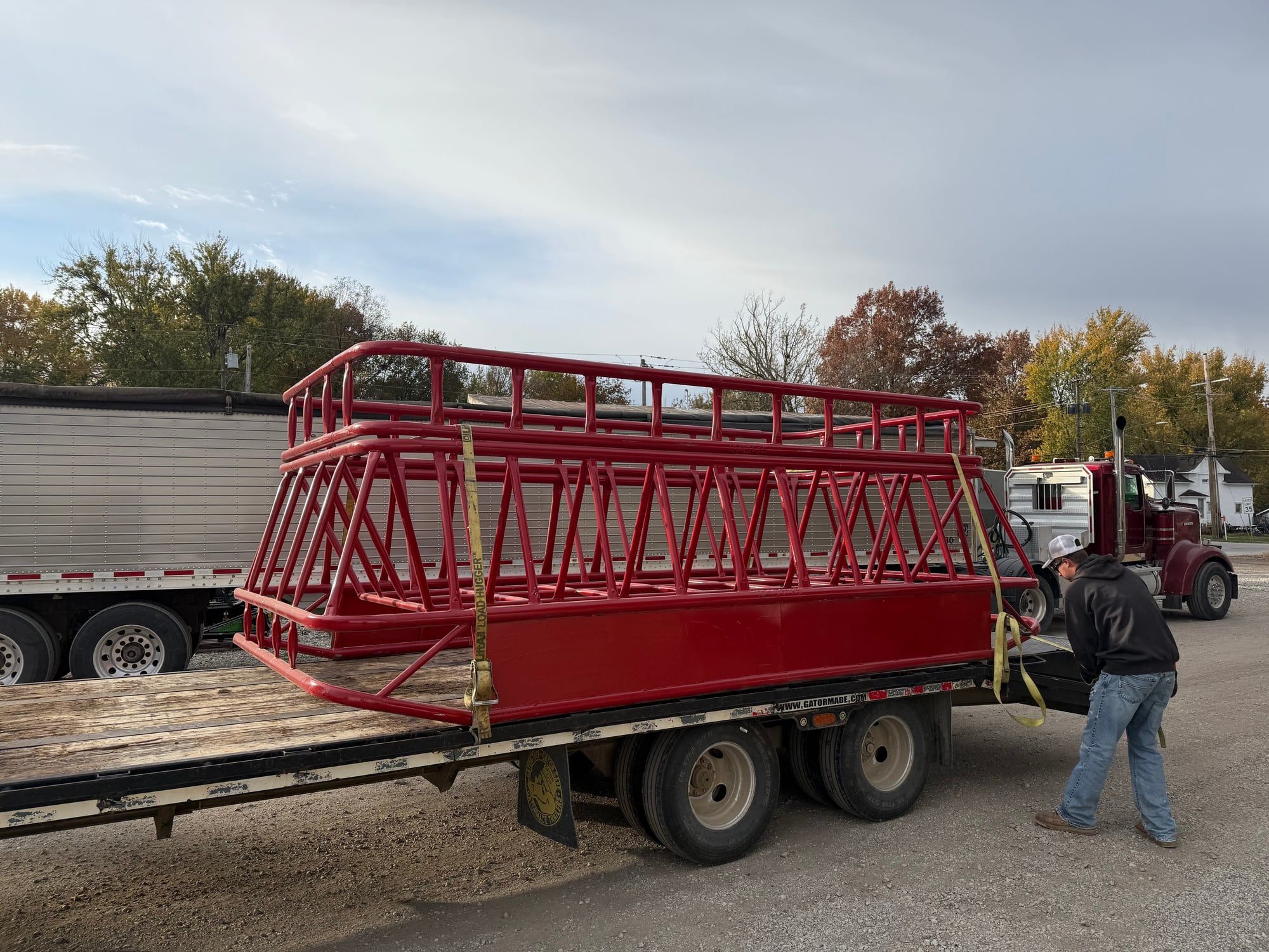 Red double bale feeder with insert loaded on a flatbed trailer
