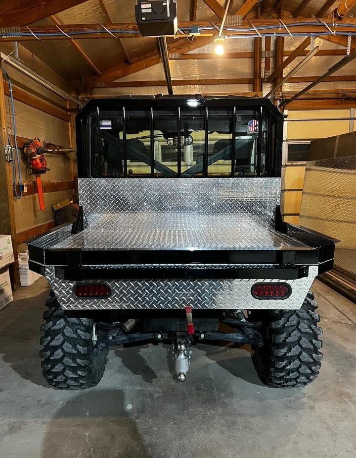 Side by side UTV with a diamond-plate aluminum flat bed, rear view in a garage