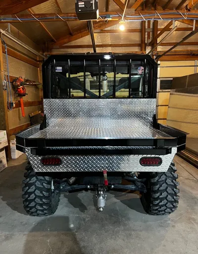 Side by side UTV with a diamond-plate aluminum flat bed, rear view in a garage