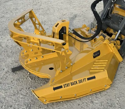 Yellow brush cutter on a skid steer with "Stay back 300 ft" warning decal