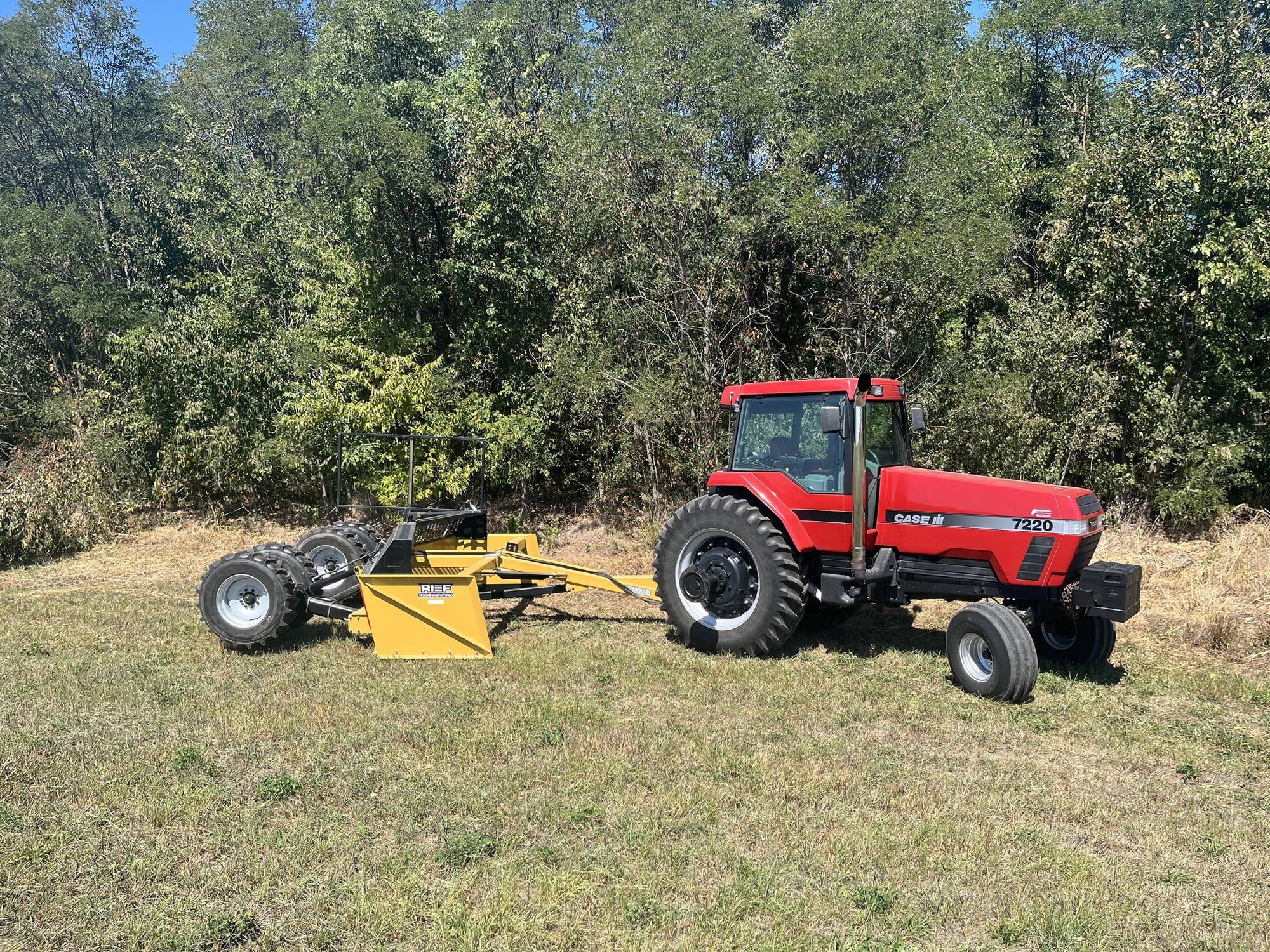 Red Case IH tractor pulling a yellow V-Shape Box Scraper from Reif Design & Manufacturing across a grass field